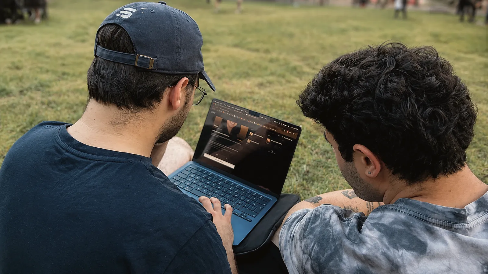 Çimde oturan iki öğrenci, EVRE seans ekranını gösteren tek bir laptopa bakıyor.