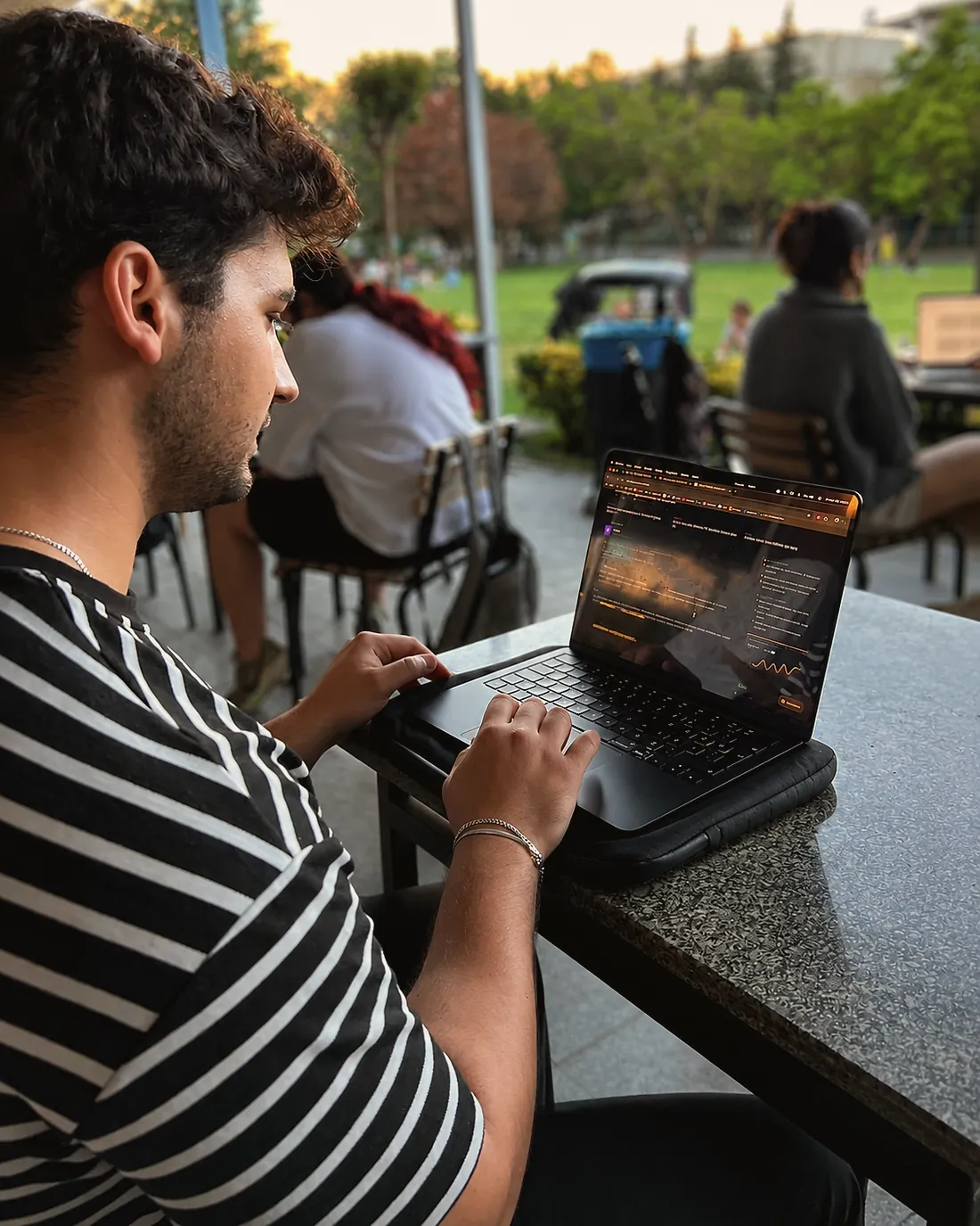 Çizgili tişörtlü bir öğrenci, açık havadaki bir kampüs masasında EVRE arayüzü açık bir laptopta çalışıyor.